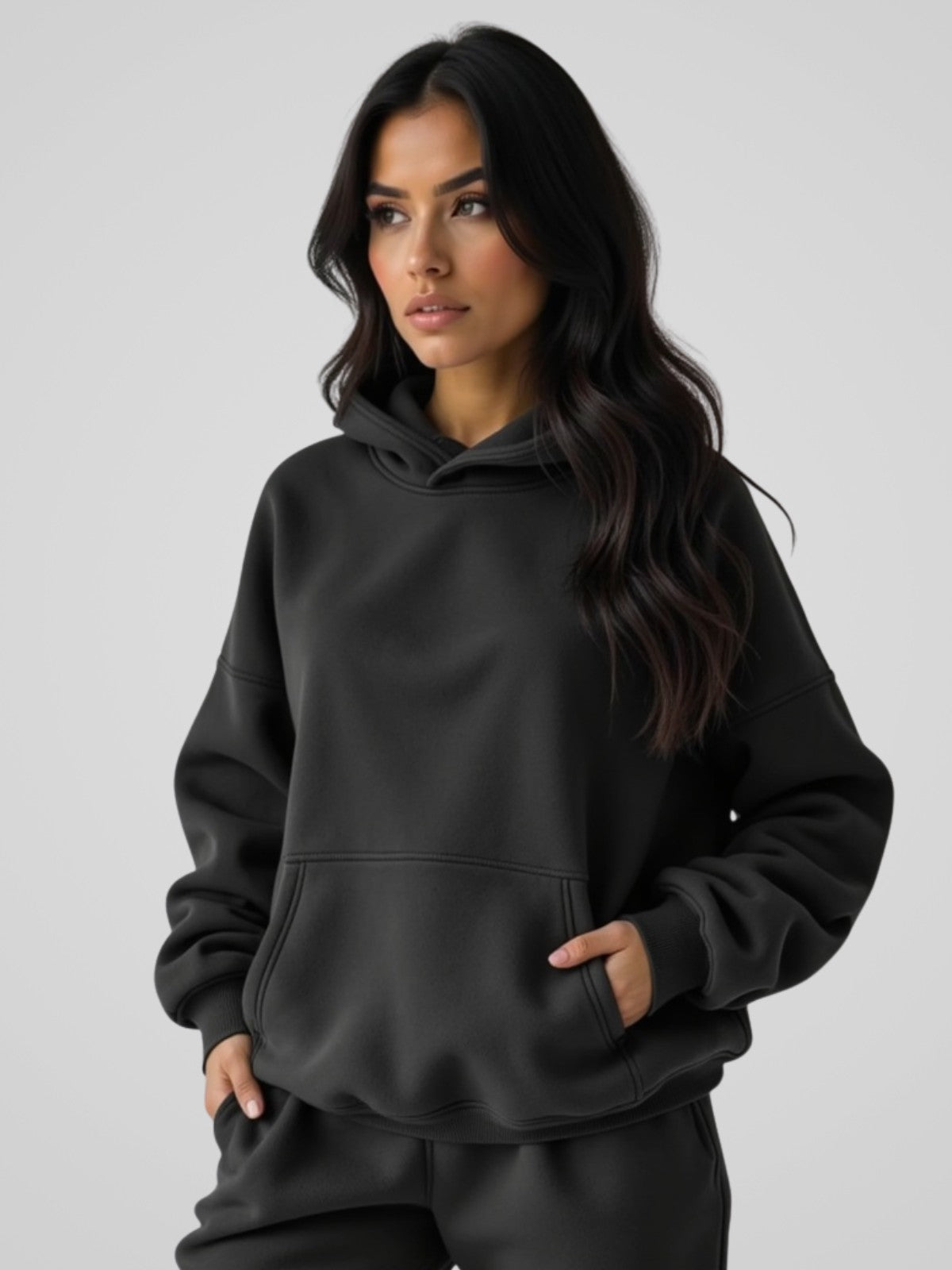 Woman wearing a black oversized hoodie, standing and facing forward to show the fit and style.