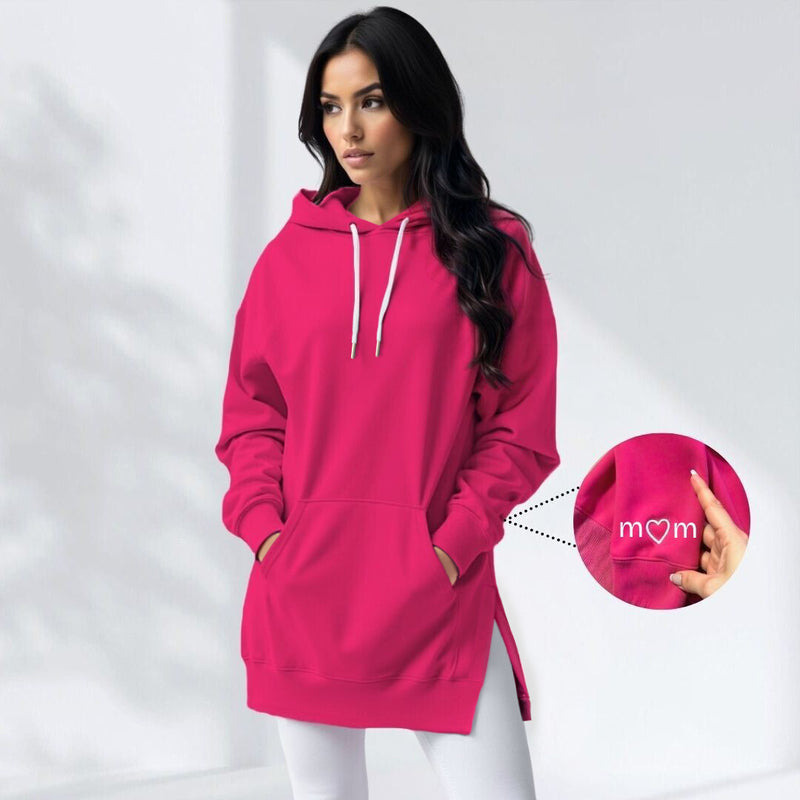 Woman wearing a pink hoodie dress with an embroidered mom heart on the sleeve, standing and facing forward to show the fit and style.